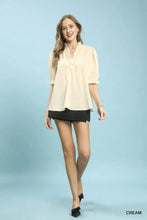 Cream-colored umgee textured check ruffle blouse with v-neck and puff sleeves featuring a ruffled neckline
