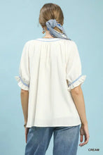 Cream-colored umgee textured split neck blouse with delicate blue embroidered trim and ruffled neck puff sleeves