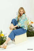A woman wears an umgee watercolor floral blouse with lace detailing and flounce sleeves paired with navy pants