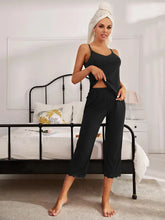 Woman wearing black v-neck lace trim slit cami and pants pajama set with adjustable strap length in cozy bedroom