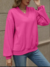 A vibrant pink v-neck solid color casual sweatshirt with stretchy material and ribbed cuffs and hem