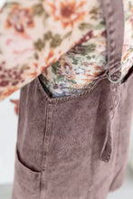 A dusty rose vintage wash denim overall dress with a floral-patterned shirt visible at the top