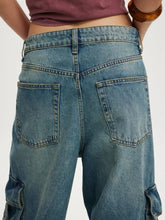 Vintage wash wide leg cargo jeans in medium-wash blue denim with visible stitching and side pockets