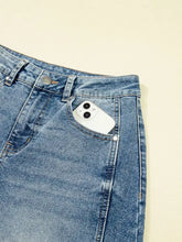 A white iphone with dual rear cameras peeking from the back pocket of blue vintage washed seam shift jeans