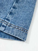 Medium-wash blue denim fabric with visible stitching on the seam of a sleeveless denim dress with western belt buttons