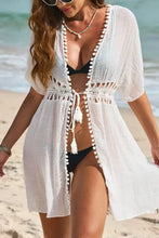 White beach cover-up with pom pom trim over black bikini