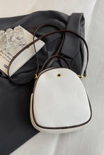 White faux leather handbag with brown trim, gold zipper, and textured crossbody design