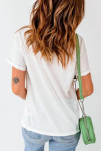 White t-shirt with orange text, rolled sleeves and green crossbody bag
