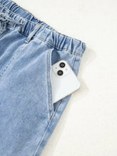 A white smartphone in the front pocket of light-wash denim wide leg drawstring raw hem jeans