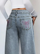 Back side of light-wash denim wide leg high waist jeans with pink embroidered bow designs on the pockets