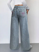 Back side of light-wash denim wide leg high waist jeans with pink embroidered bow designs on the pockets