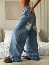 Back side of light-wash denim wide leg washed jeans with distressed ripped patches on back pockets and wide-leg silhouette