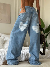 Light-wash denim jeans with distressed ripped knee patches featuring a wide-leg silhouette and relaxed fit
