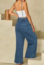Woman in white camisole and wide leg denim overalls with adjustable tie straps