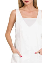 White sleeveless top with square neckline and front pockets paired with a washed adjustable strap denim overall dress